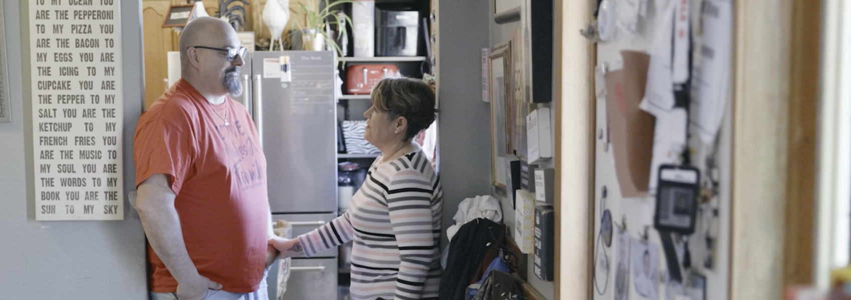 Foster parents stand and talk in the doorway of their busy home